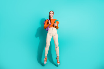 Portrait of lovely woman with foxy hairstyle wear orange crop top hold rucksack copybook jumping isolated on turquoise color background
