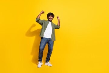 Portrait photo of funny young hispanic winning lottery raised fists up guy in khaki shirt isolated on yellow color background