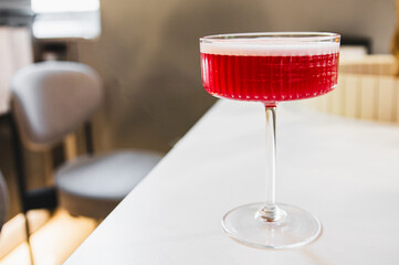 A vibrant red cocktail in a classic stemmed glass, placed on a white bar counter, with a soft-focus...