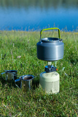 Close-up of a boiling kettle on a camping gas burner in green nature. Making a hot drink while hiking. Concept of tourism