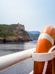 Lifebelt hangs on the railing of a ship journeying to Port de Sóller, with Torre Picada watchtower in the background, providing an essential element of maritime safety, travel and coastal tourism.