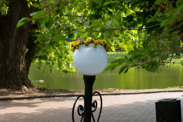 A lantern lighting in the park with a wreath of dandelions. Lighting of the park area