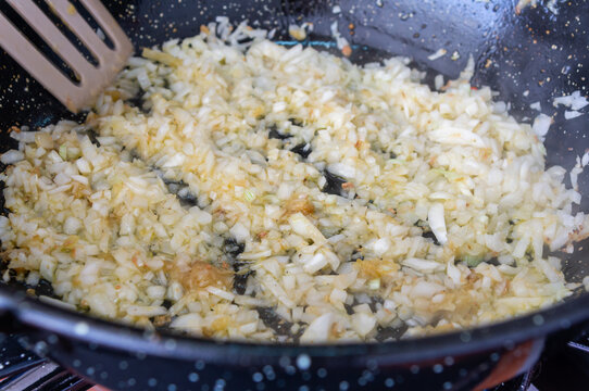 Homemade Aromas: Preparing Onion and Garlic Sofrito in Pan with Wooden Spoon.