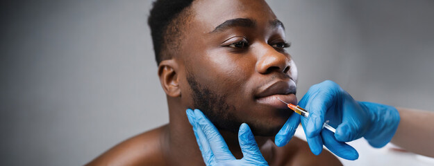 A man receiving a cosmetic lip injection administered by a professional in a clinical setting, highlighting modern beauty treatments and medical care.