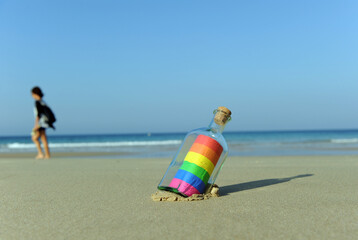 LGTBQ pride message in a bottle on the seashore. Defocused person walking on the beach