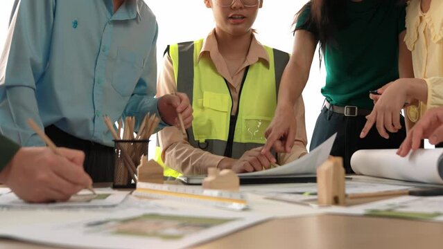 Smart architect and safety engineer discussion about building blueprint on table with architectural document, measurement tools and wooden block scatter around at modern office. Closeup. Delineation.