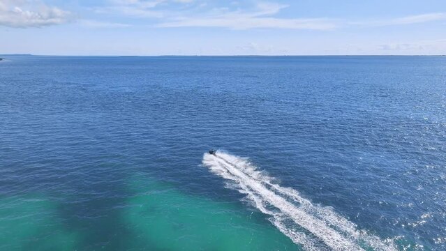 Aerial view of the jet ski in clear blue water on summer sunny day. Top drone view of fast floating motorboat in ocean ocean. Travel in Zanzibar. Tropical landscape with motorboat on the sea. Travel