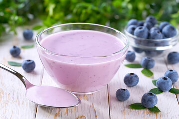 blueberry smoothie in a bowl with spoon and fresh blueberries on a white table, selective focus.