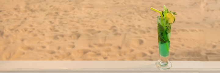 Banner of tropical green cocktail with straw, mint and lime on background of golden sand. the concept of relaxing and eating by the sea on a bright, hot and sunny day on the beach. soft focus. copy