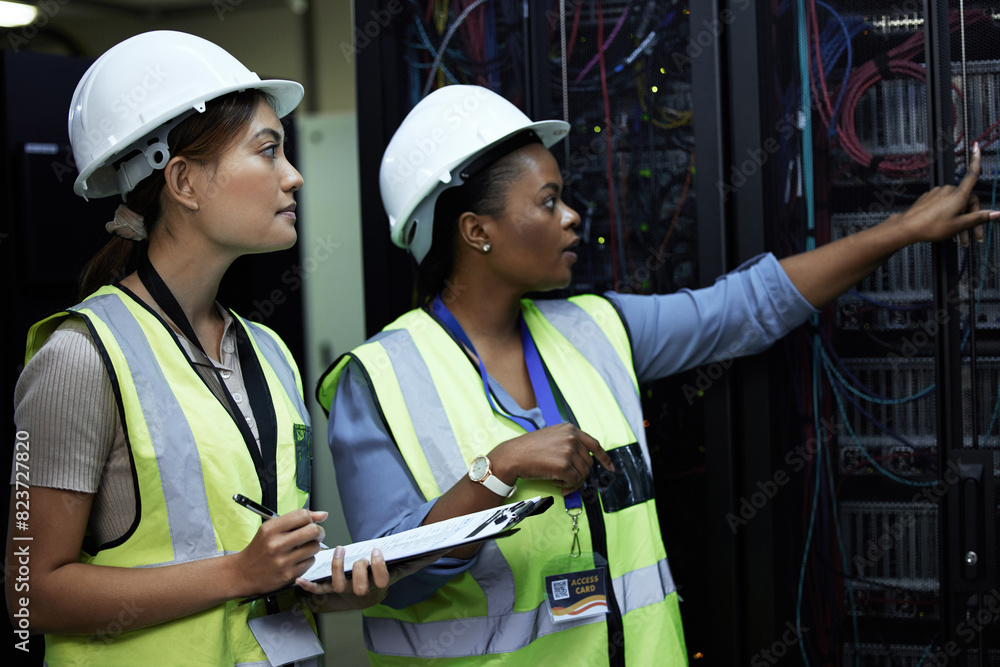 Fototapete Inspection, women and data engineer with pointing in computer center for teamwork or collaboration. Female people, clipboard and tech hardware security in server room for system update or maintenance