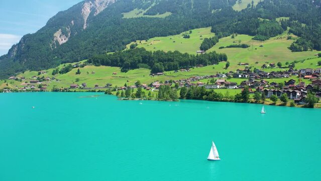Drone footage of turquoise clear lake Lungern or Lungerersee in Switzerland in summer sunny day with village and green meadow