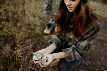 A young woman performing a ritual with a rock in hand while a man stands behind her observing in nature