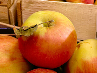 A ripe, fresh yellow-red apple with a close-up leaf on the background of apples and a wooden box. Proper nutrition, vitamins and trace elements. Fruits are rich in iron. Supermarkets and shops. Photo.
