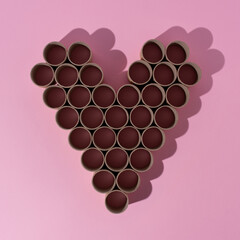 Empty toilet paper rolls with heart shaped shadow on pink background. Minimal layout pattern.