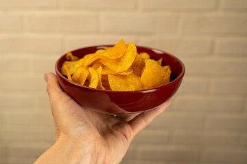 A hand holding a red bowl filled with potato chips