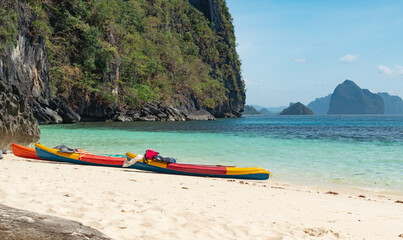 Colorful kayaks resting on sandy beach near rocky cliffs on a sunny day