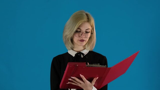 Female student holds folder checking papers on blue background. Young woman expresses dissatisfaction due to missed sheet