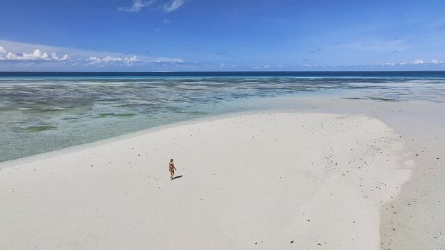 Aerial view of walking alone young woman on the sandbank in ocean, white sandy beach, blue sea in low tide at sunny summer day in Nakupenda, Zanzibar island. Top view of girl, sand spit, water, sky