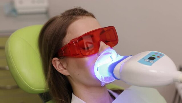 Patient eyewear, Cosmetic dentistry, Dental hygiene. In dental clinic, patient with protective eyewear is receiving teeth whitening treatment using blue light device.