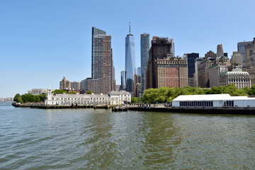 A New York skyline with a large building in the middle. The water is calm and the sky is clear