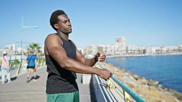 A young man stretching outdoors by the seaside promenade under clear skies.