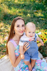 Fototapeta premium a young mother with a baby plays and cuddles in nature in summer on a green lawn, happy motherhood, mom on maternity leave