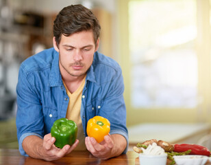 Choice, man and peppers in kitchen for cooking, food preparation and thinking at home. Decision, vegetables and male private chef in house with comparison, options and preference for flavor for dish