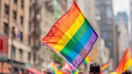 Closeup of the rainbow flag waving in front, with people celebrating and cheering at an outdoor pride event. The crowd is blurred against the backdrop of city buildings, in the style of no artist.