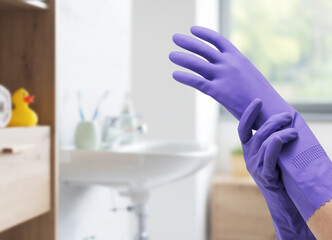 Hands wearing cleaning gloves and bathroom in the background