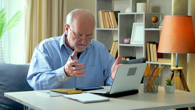 An elderly businessman, gray-haired in a blue shirt, at his desk, reads the data from an accounting report, communicates with employees, finds inaccuracies, showing obvious displeasure. Slow motion.