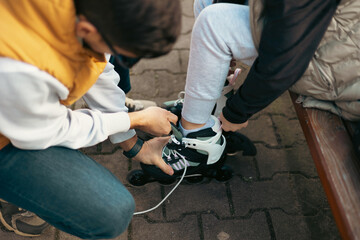 Dad helps his daughter put on skates. Parents and children playing sports together. Girl on roller skates