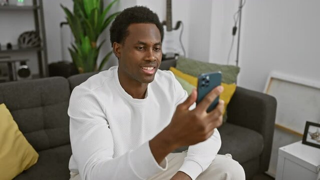 A smiling man uses a smartphone in a modern living room, signaling relaxation and connectivity.