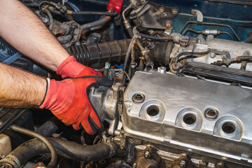 The mechanic is reassembling the distributor.  Replacing a rubber gasket. Valve cover, air filter intake pipe, ignition coil.