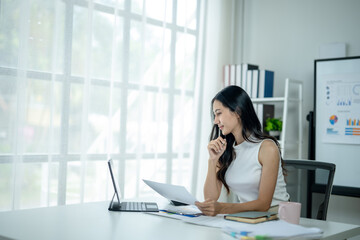 A woman is sitting at a desk with a laptop and a piece of paper in front of her