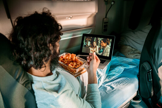 Man watching movie on laptop in truck sleeper cabin with snacks