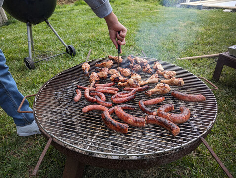 Cozinheiro a assar carne e salsichas no assador na grama do quintal, churrasco no fim de semana, festa com piquenique ao ar livre