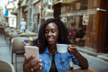 African American woman enjoying coffee and using smartphone at a cafe