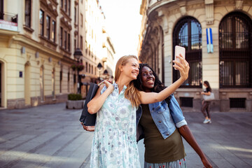 Two diverse female friends taking a selfie together in a city street