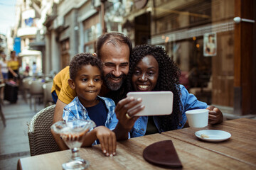 Happy multiracial family taking a selfie at an outdoor cafe