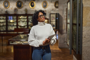 Thoughtful young woman wearing glasses and looking at exhibition. Concept of Museum Day