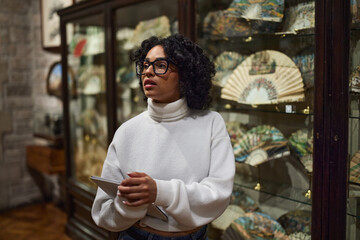 Thoughtful young woman wearing glasses and looking at exhibition. Concept of Museum Day