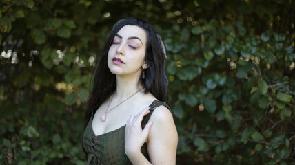 a fantasy portrait of a young beautiful fairy woman with long dark hair and dreadlocks and pale skin wearing green being playful in a forest holding hands up to touch the trees