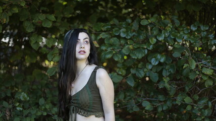 a fantasy portrait of a young beautiful fairy woman with long dark hair and dreadlocks and pale skin wearing green being playful in a forest holding hands up to touch the trees