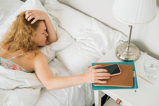 Woman turning off alarm on her phone while lying down in bed