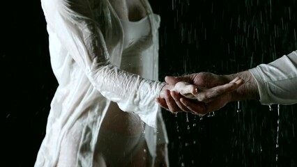 In the rain and in the dark, a close-up of the hands of a man and a woman intertwining on a black background conveys their passionate intimacy and openness of souls.