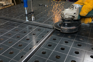 on a metal table for welding, the part lies clamped in a vice, the master is processing the part,...