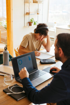 Father working on laptop and son doing homework at home