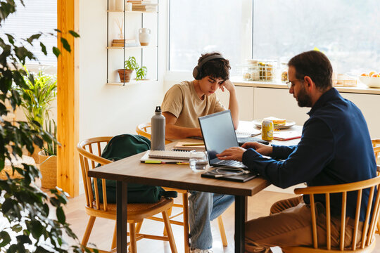 Father working on laptop and son doing homework at home
