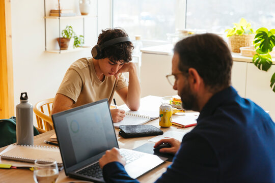 Father working on laptop and son doing homework at home
