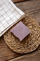 A piece of natural soap and white checkered towel on wooden background. Lavender soap. Top view